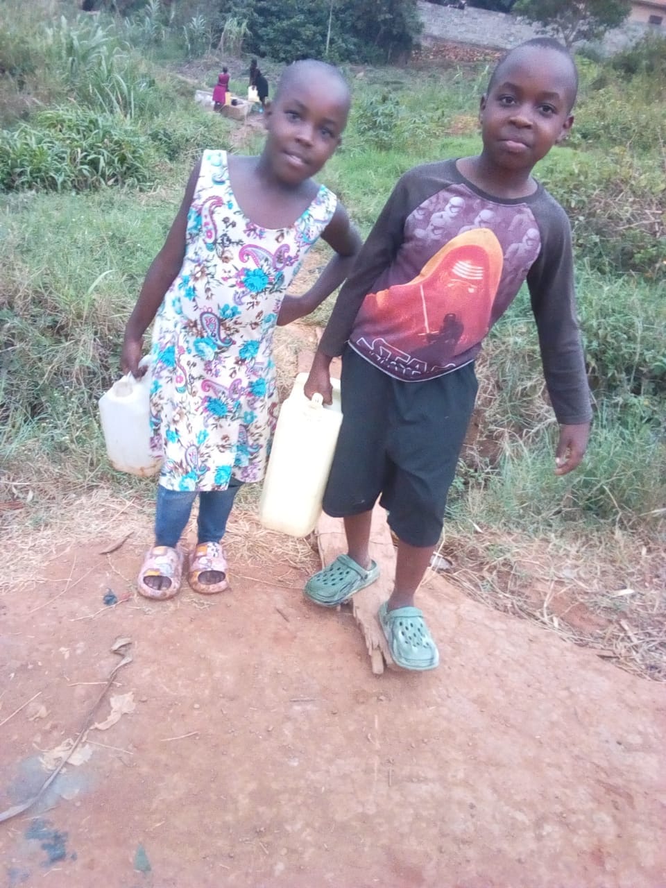 Children carrying water home along a path near Kikyamuzi